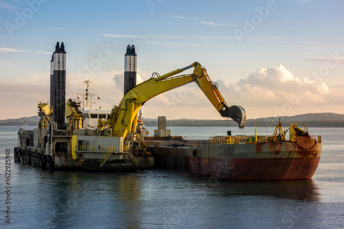 Slika na platnu Large Dredging Vessel with Hydraulic Excavator Unloading Sediment into Barge at Sea