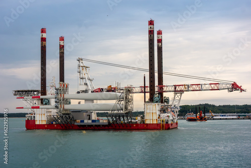 Offshore Wind Turbine Installation Vessel with Giant Crane and Turbine Blades at Sea. Renewable Energy Logistics, Industrial Maritime Engineering and Green Energy Transition Concept
