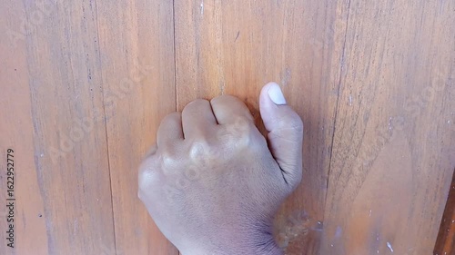 Portrait of a woman's hand knocking on the wooden door of a house.