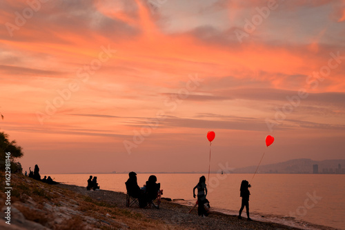 Fototapeta Naklejka Na Ścianę i Meble -  silhouettes of kids with baloons on the beach at sunset