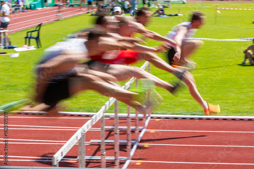 runners crossing the hurdles in a decathlon - blurred