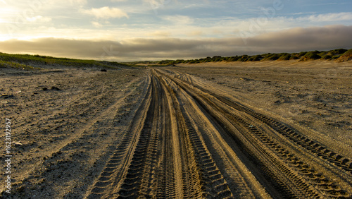 Tire tracks on sandy beach landscape at sunset, showcasing natural textures and patterns, with gentle waves in the distance and a serene atmosphere of tranquility and exploration