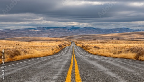 Empty highway stretches into a vast, autumnal landscape under a dramatic sky