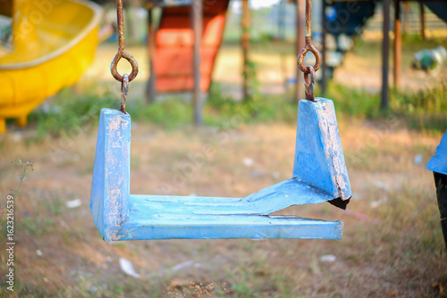 Broken plastic children's swing on the playground, old and unsafe swing. Old blue swing in an abandoned outdoor playground rustic environment