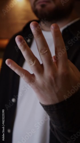 Man holding four fingers. Casual outfit, wearing shirt in a dimly lit room