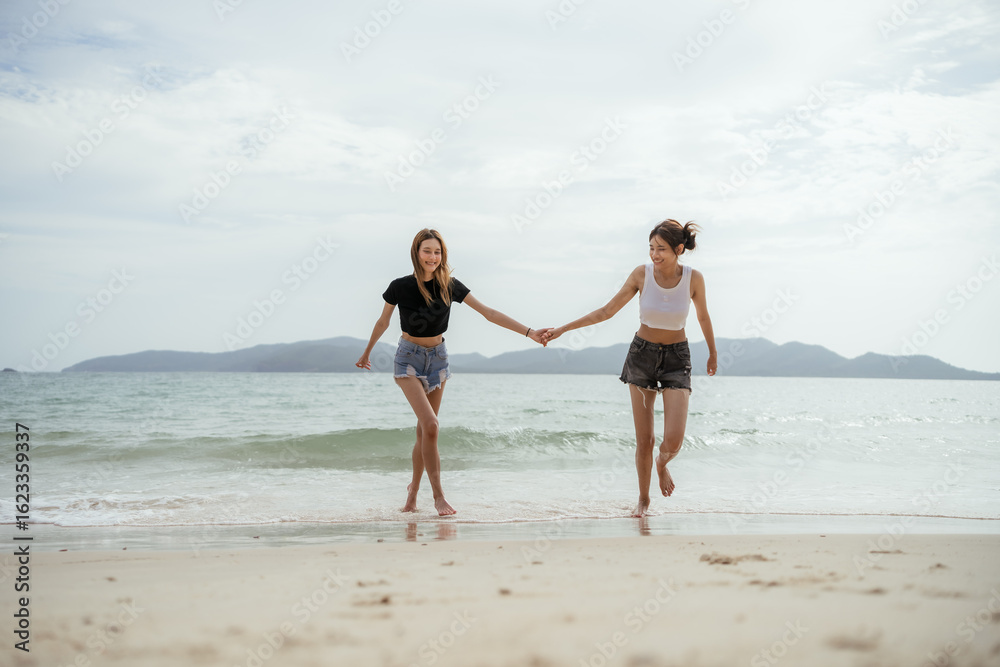 Two women are running on the beach. One of them is wearing a black shirt and shorts. Two female friends holding hands and walking on the beach, enjoying a summer vacation together. Two women are running on the beach. One of them is wearing a black shirt and shorts. Two female friends holding hands and walking on the beach, enjoying a summer vacation together.