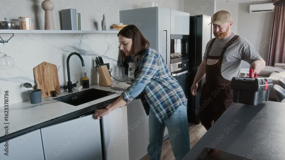 Medium shot of young woman leading plumber or repairman to kitchen sink at home and walking towards camera Medium shot of young woman leading plumber or repairman to kitchen sink at home and walking towards camera