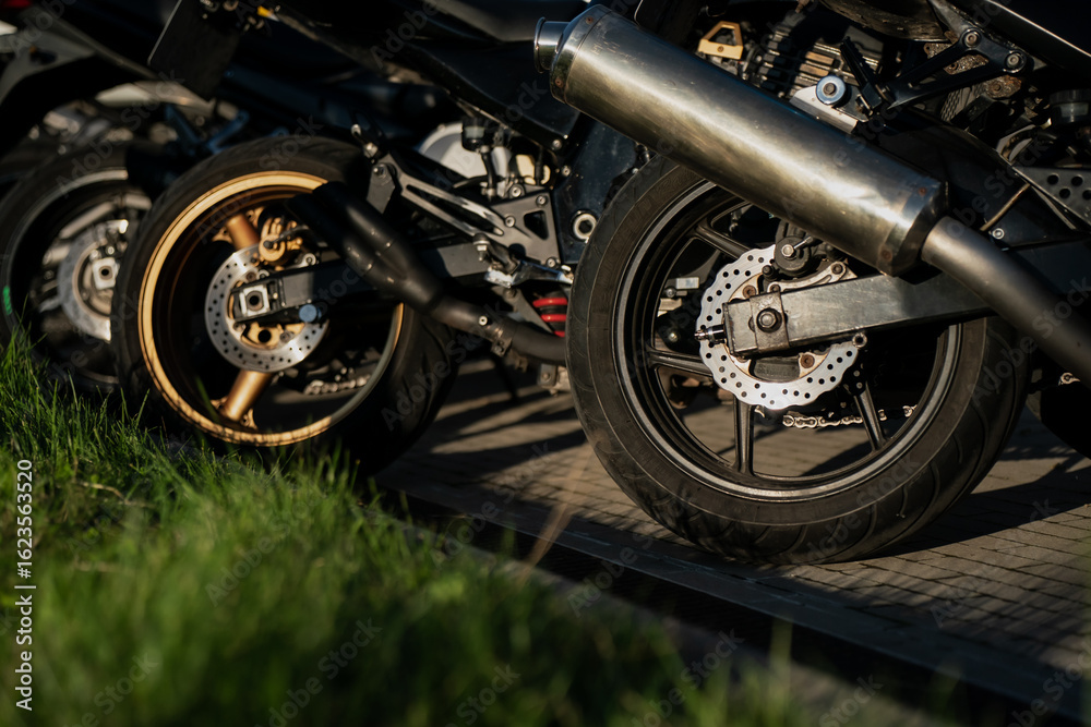 Obraz premium Motorcycle rear wheels with visible disc brakes and exhaust pipes parked on paved lot at outdoor gathering showcasing sportbike design, suspension, and modern braking technology