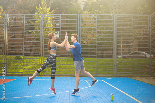 Young couple of guy and girl have fun together on sports ground, fitness outdoors, concept of cooperation and teamwork in pairs