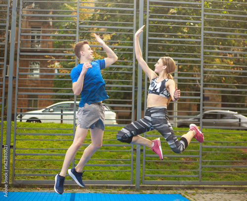 Young couple of guy and girl have fun together on sports ground, fitness outdoors, concept of cooperation and teamwork in pairs