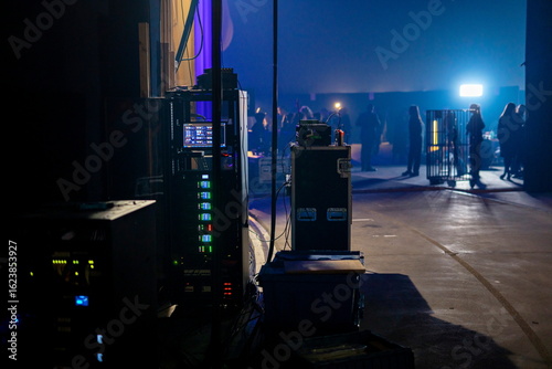 Professional audio visual production equipment and control systems in backstage area with blue lighting and crew