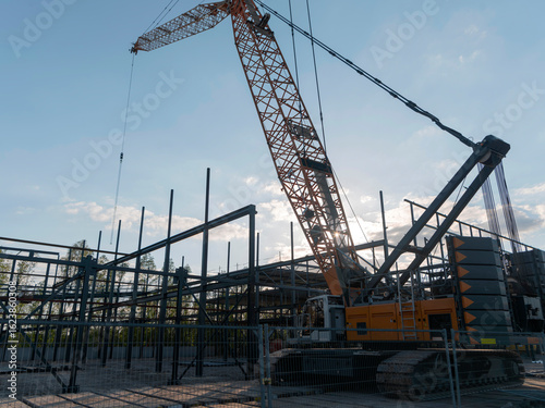 Large construction crane working on steel building framework against cloudy sky background