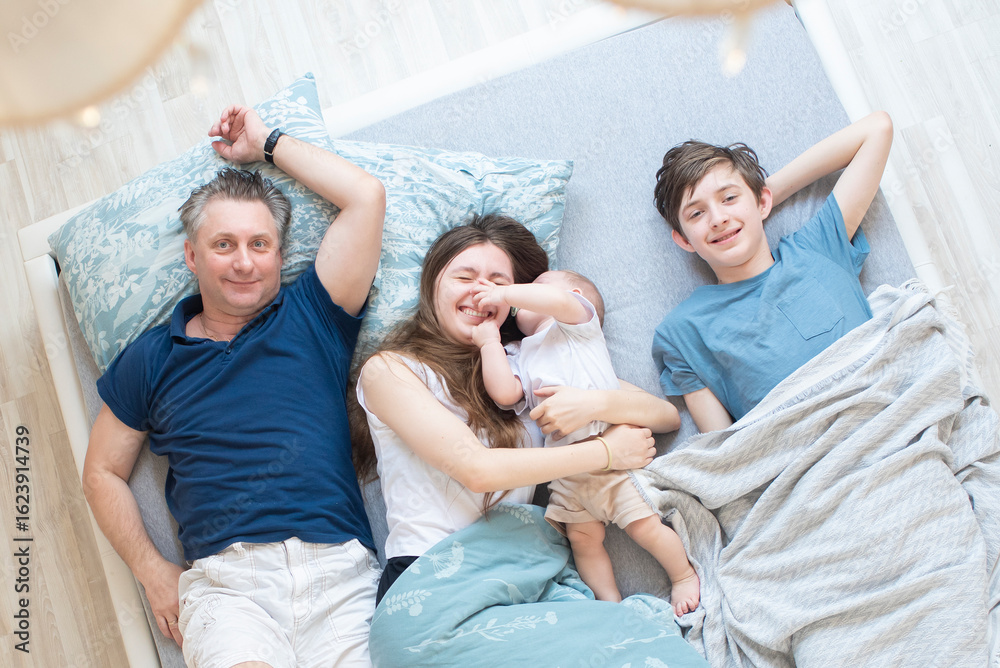 Obraz premium father and three children lying in bed, having fun in the morning, top view