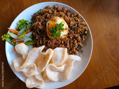 A delicious plate of Indonesian Nasi Goreng (fried rice), served with a fried egg, crispy prawn crackers, and fresh pickles. A famous and popular dish from Indonesia.
