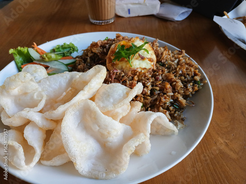 A delicious plate of Indonesian Nasi Goreng (fried rice), served with a fried egg, crispy prawn crackers, and fresh pickles. A famous and popular dish from Indonesia.