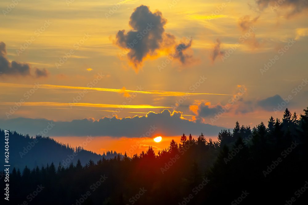 Naklejka premium Stunning sunset over a forest landscape with colorful clouds reflecting on the horizon