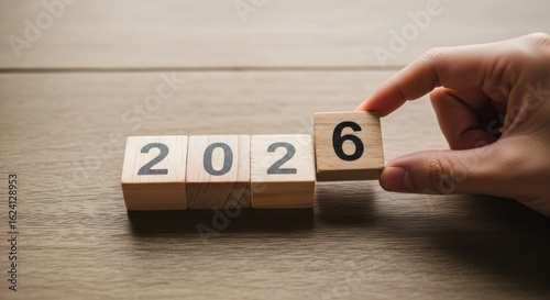 Hand placing wooden block with '6' to form '2026'