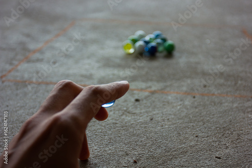Photography A person playing a game of marbles, aiming to shoot at a group of marbles in a square