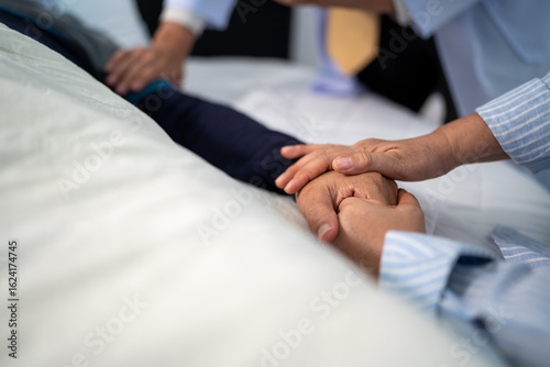 scene of bedridden patient, focus on hand of wife holding hands illness elderly hopeless senior man. home caregiver nurse visit retirement patient for health check up recovery process medical service