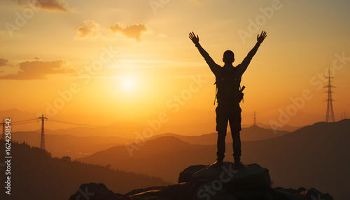 Silhouette of a person at Sunset on the mountain: A person stands on a mountain at sunset with arms outstretched, celebrating a sense of freedom, achievement and success.