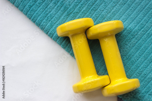 Bright yellow dumbbells are placed on a textured teal mat, showcasing a vibrant fitness environment ideal for exercising and strength training.