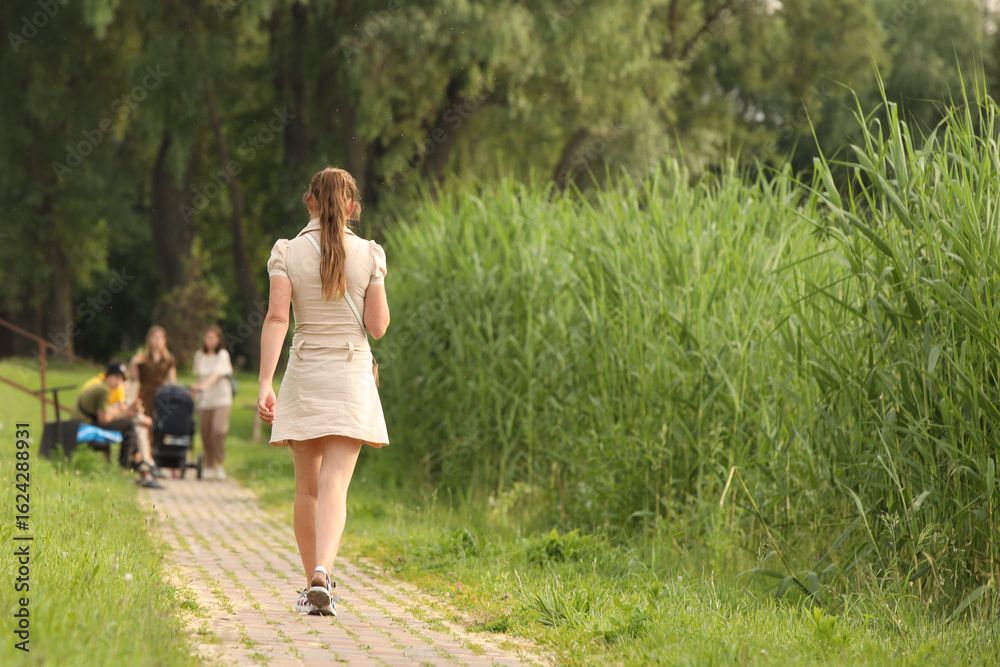A young girl in a revealing outfit with bare legs walks along a park alley among the greenery to meet her friends. Fashion of modern youth. A young girl in a revealing outfit with bare legs walks along a park alley among the greenery to meet her friends. Fashion of modern youth.