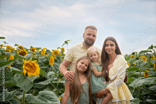 A photo of a happy family, parents and daughters smiling together in a sunflower field.