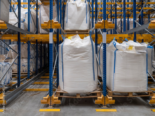 Large white bulk bags stored on pallets in industrial warehouse with multi-level racking system