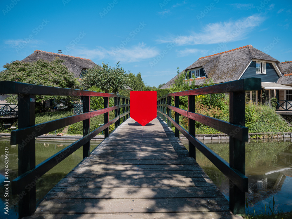 Obraz premium Physical red shield on wooden bridge with village backdrop for scenic branding applications