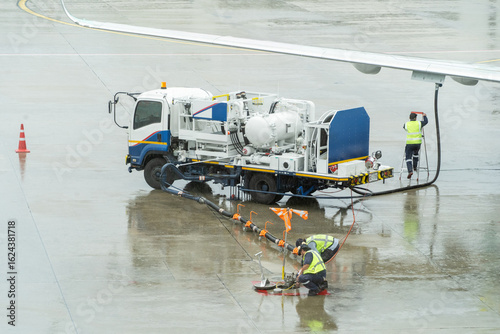A man in a yellow vest is filling a plane with fuel