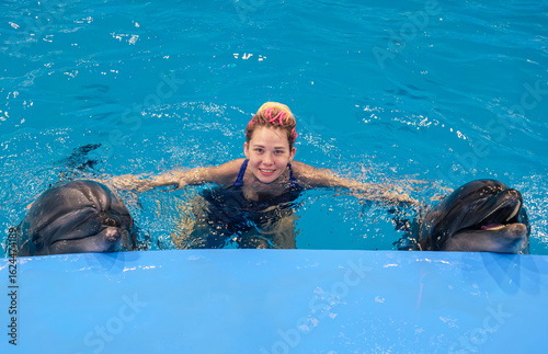 Vászonkép Woman interacts with dolphins in a blue pool during a marine park encounter