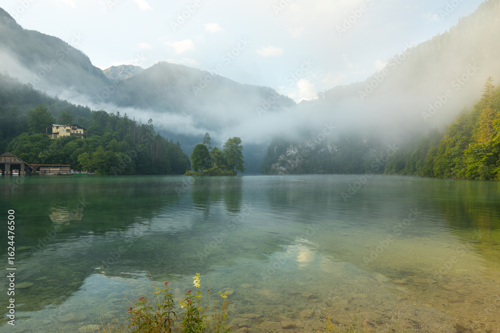 Naklejka premium Mystischer Morgen am Königssee in Schönau mit Bootshäusern und Christlieger. Sonnenaufgang und schöne Nebelschwaden über dem Königssee im Kessel.