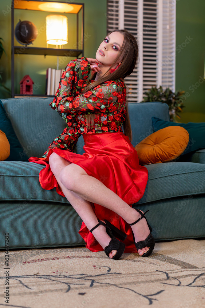 Obraz premium An Elegant Woman in a Stunning Red Dress Posing Gracefully on a Stylish and Cozy Sofa