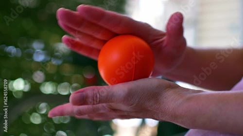 Close up footage on middle aged woman's hands holding an anti-strees orange rubber ball and playing with it. Selective focus, nice soft background. 