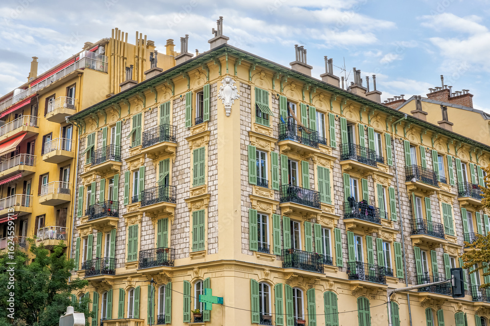 Fototapeta premium Historic building in Nice, France, with vibrant yellow facade and green shutters, showcasing intricate architectural details and balconies, capturing the essence of coastal charm