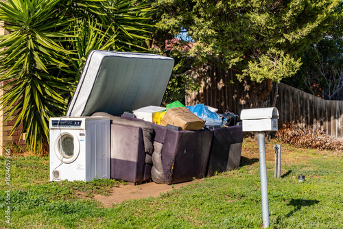Foto Hard rubbish left on the front yard garden of a suburban property featuring an old washing machine, broken furniture, mattresses, and discarded household items