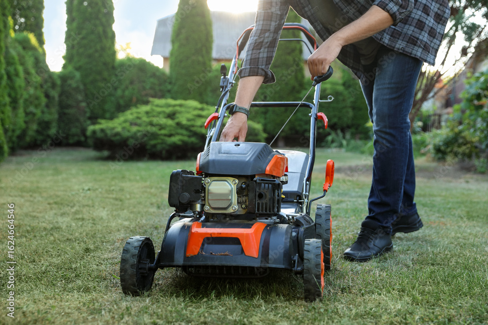 Man pulling starter cord of lawn mower in garden, closeup Man pulling starter cord of lawn mower in garden, closeup