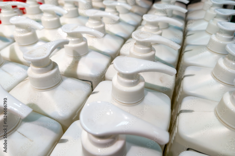 Obraz premium Rows of white dispensing bottles arranged neatly on a shelf in a retail store, showcasing various liquid products ready for customers