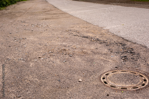 Φωτογραφία Damaged asphalt road with manhole cover and gravel needs repair