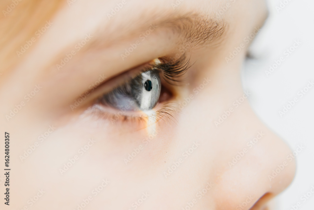 Obraz premium Close-up of a child's eye showcasing detailed iris and eyelashes, with soft lighting illuminating the eye, emphasizing vision health and the importance of regular eye examinations for children
