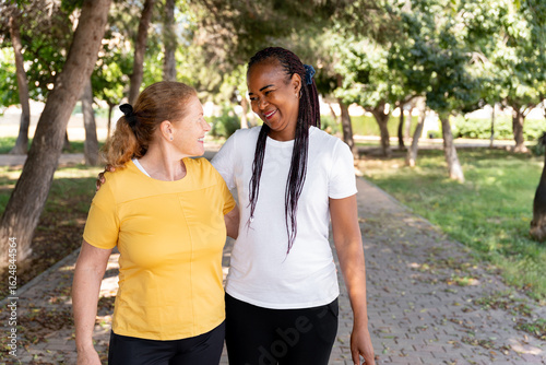 Konstfotografi Female friends walking together in urban park, sharing animated conversation and