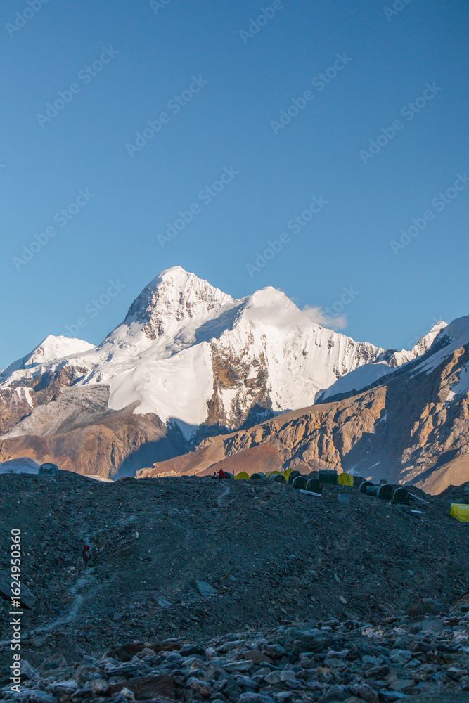 Fototapeta premium A line of tents on a rocky ridge with a breathtaking view of majestic snowcapped mountains in the background under a clear blue sky