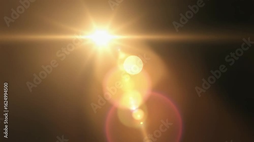 Golden sunbeam shining brightly, creating an optical lens flare with warm bokeh effects against a dark background.