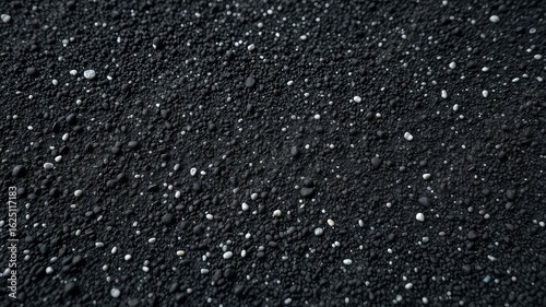 Monochromatic surface with small dark pebbles and scattered lighter flecks creating a textured and granular appearance
