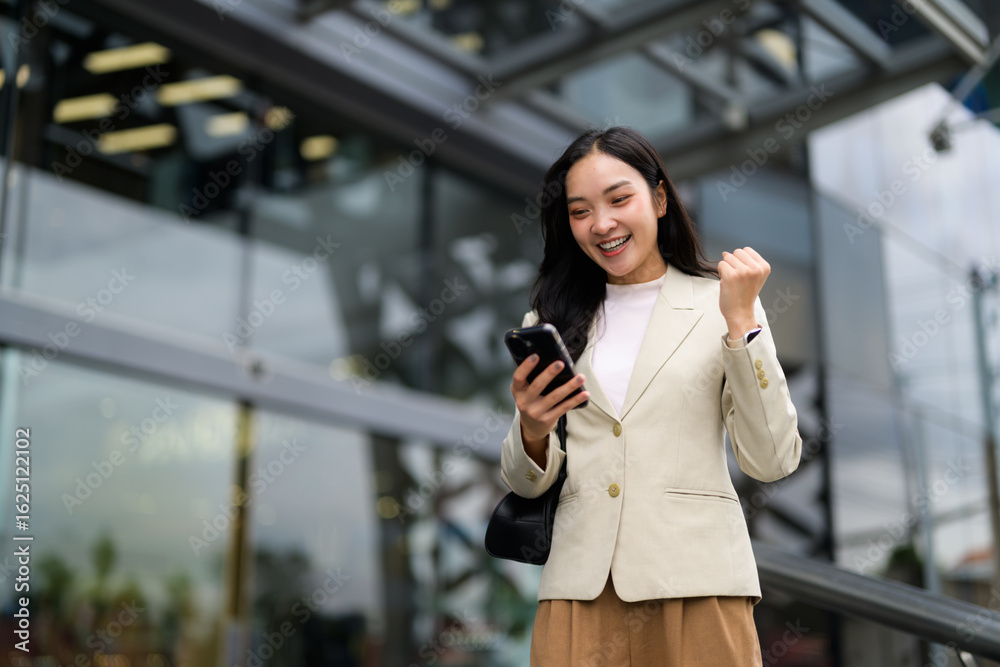 Fototapeta premium Young asian manager expressing joy and excitement after receiving good news on her phone