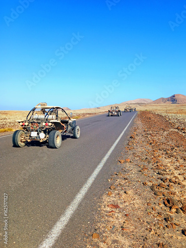 A row of buggy vehicles on the road in the middle of the desert and volcanic area of Fuerteventura. Adventure sports and fun.