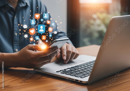 Photo of person holding a smartphone with social media icons emanating, while using a laptop, representing digital connectivity, online interaction, and modern communication strategies