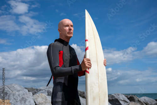 Photography surfer standing on a beach holding a surfboard wearing a wetsuit