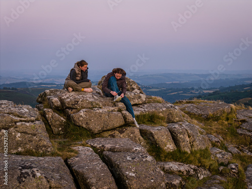 Family hiking on Dartmoor tors at sunset, silhouetted against dramatic skies in scenic moorland landscape
