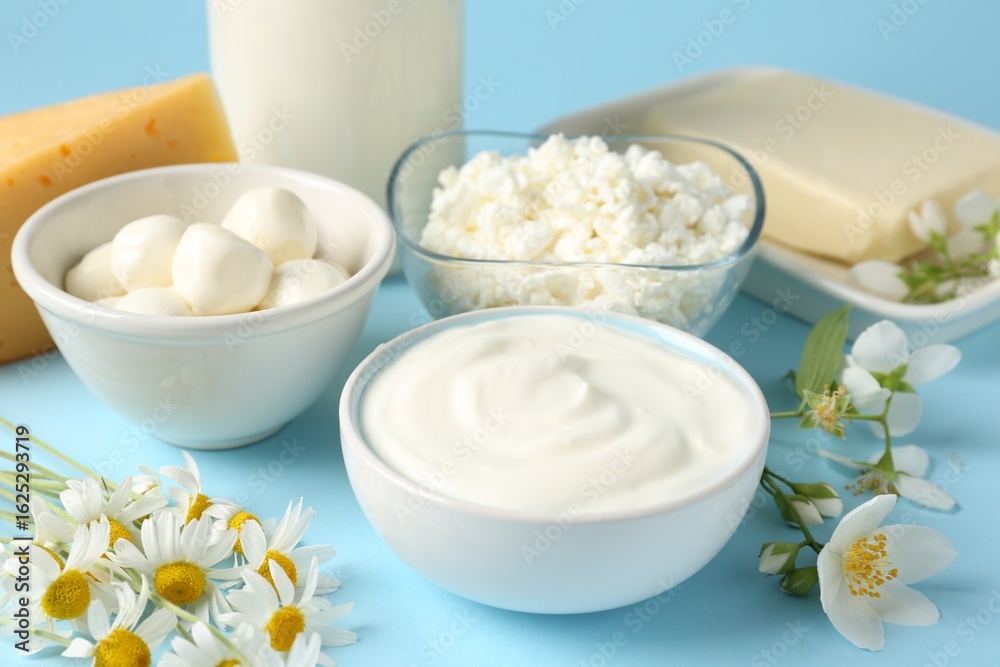 Fresh dairy products and flowers on light blue background, closeup